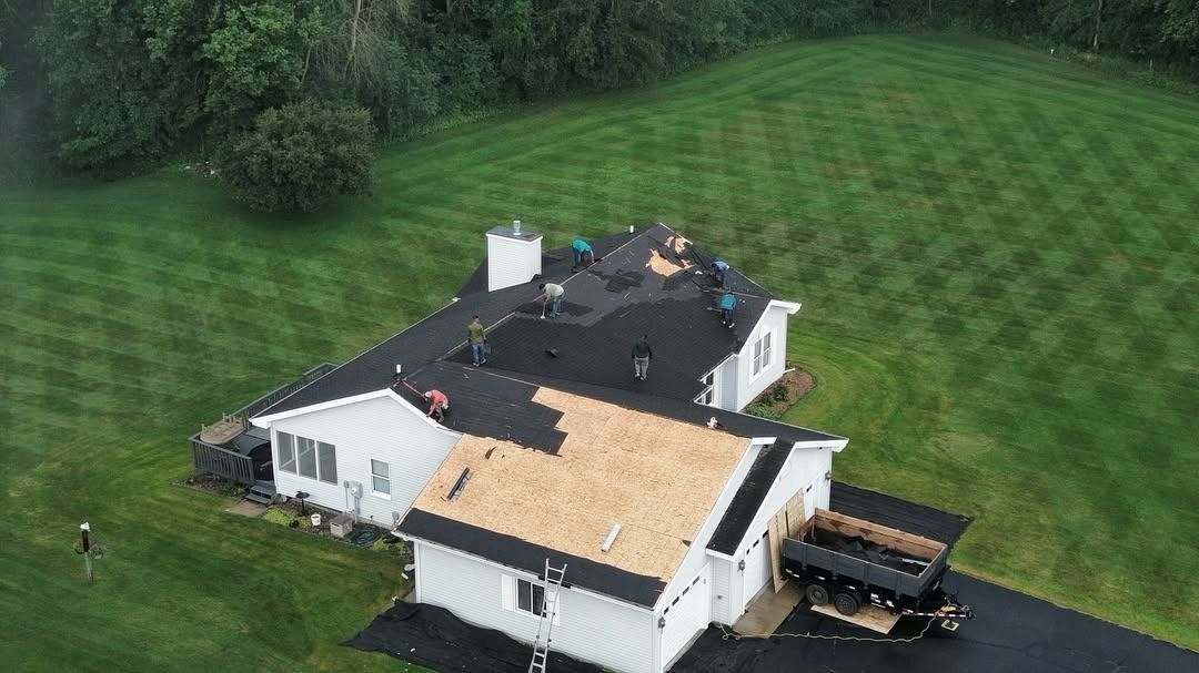 Aerial view of a white house with a black roof and tan deck, surrounded by a large green lawn.