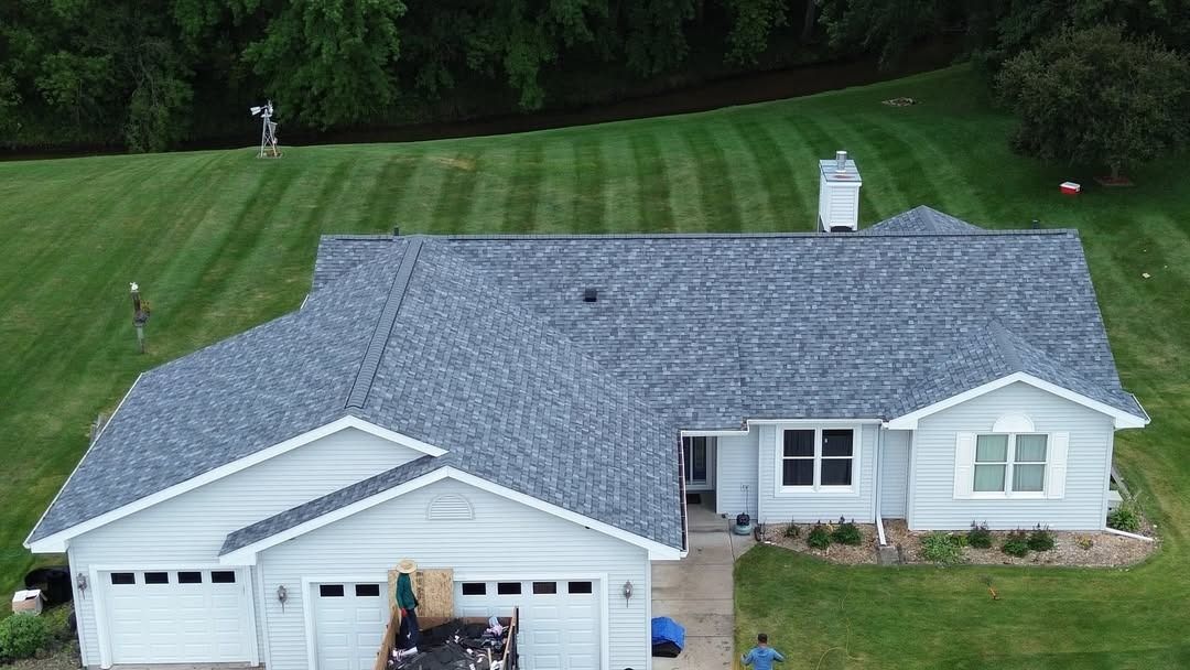 Aerial view of a white house with gray roof, attached garage, and a large green lawn.