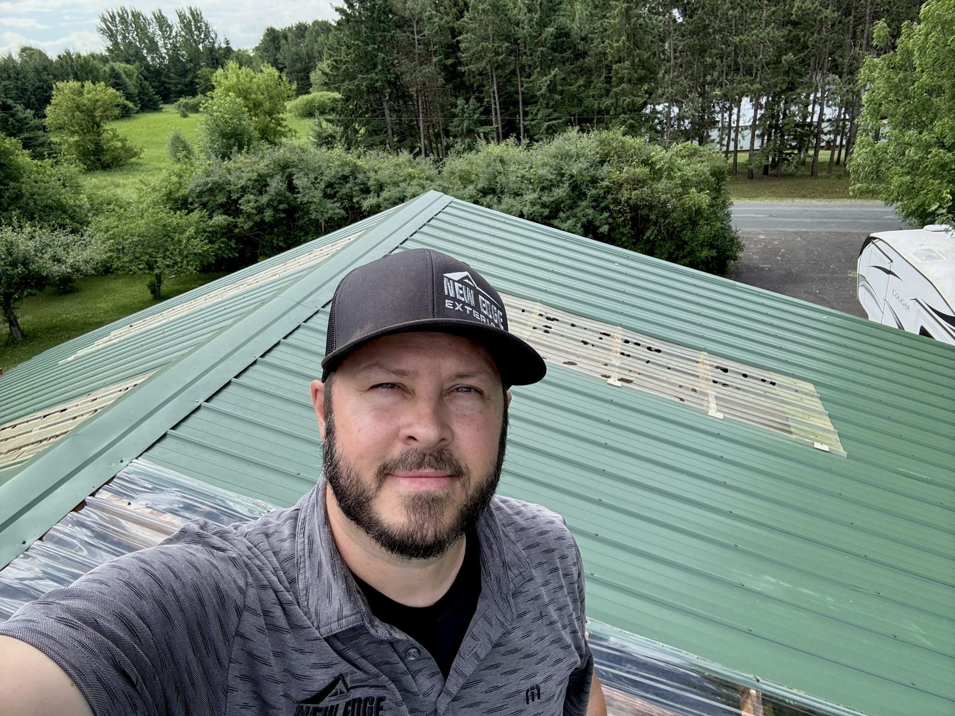 Selfie of a man on a green metal roof with trees and a driveway in the background
