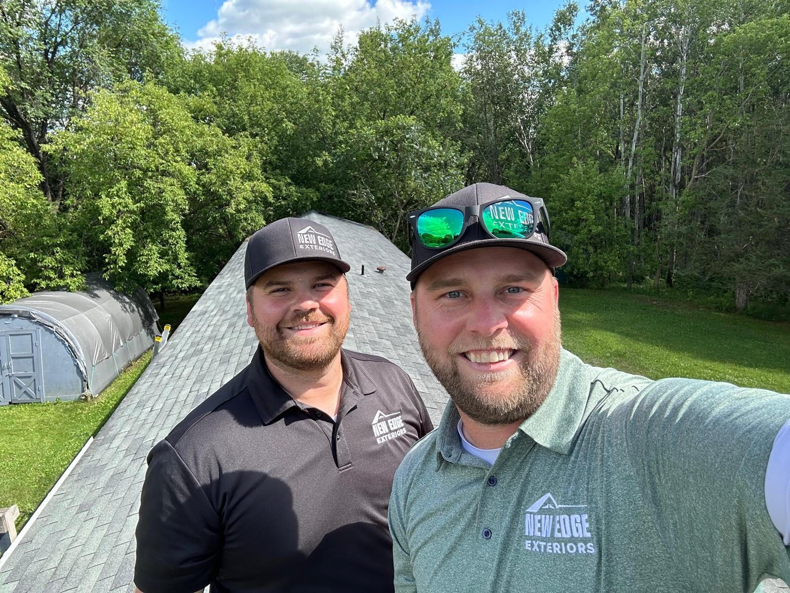 Two smiling men posing outdoors by tents and trees on a sunny day