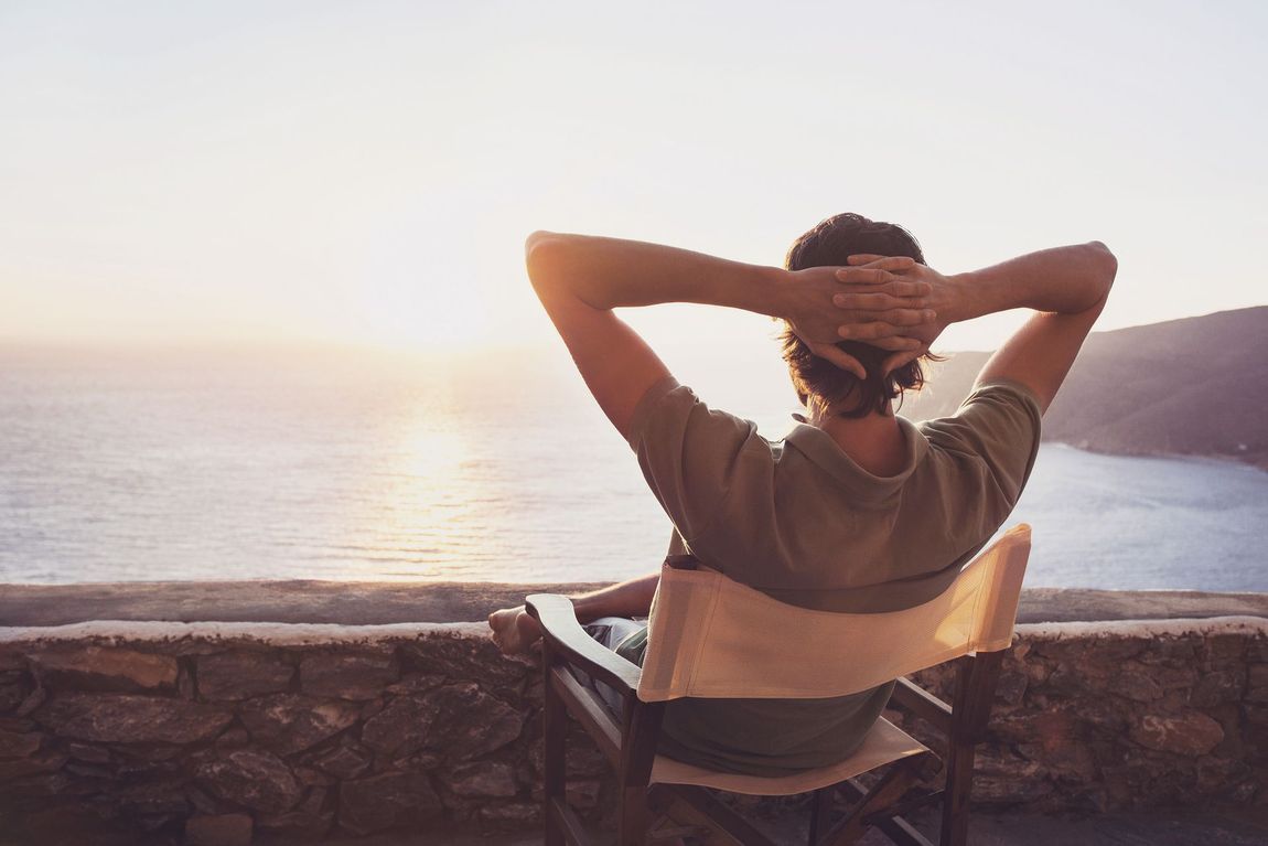 A man is sitting in a chair with his hands behind his head looking at the ocean.