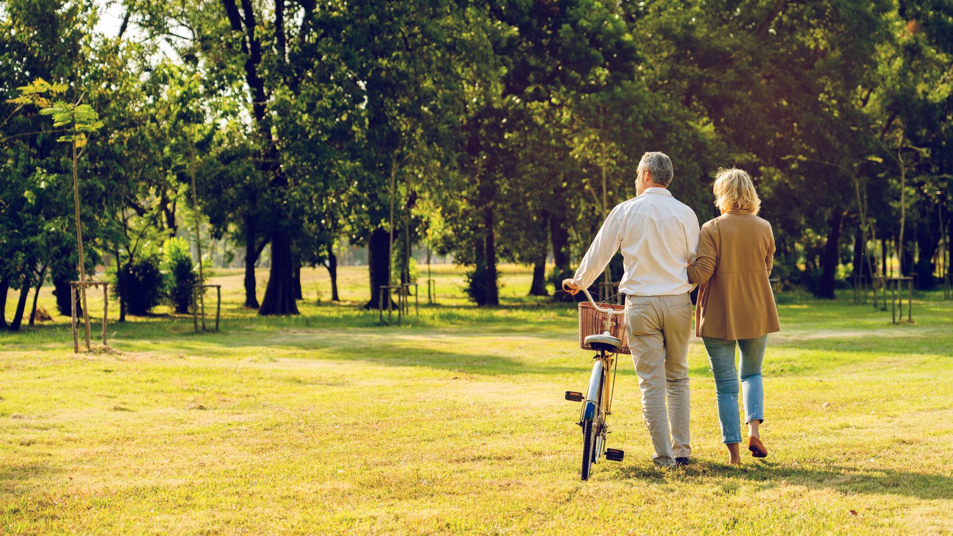 An elderly couple is walking in a park with a bicycle.