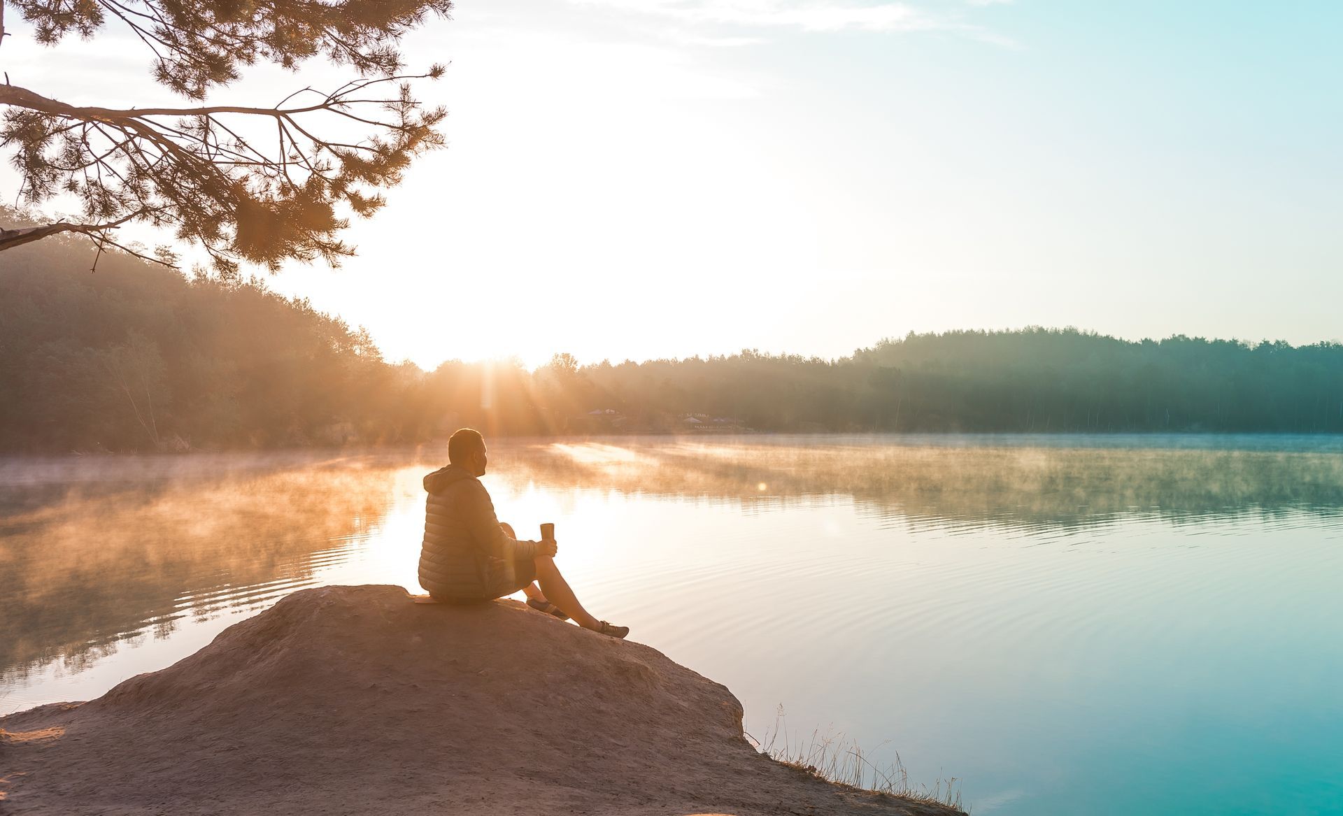A person is sitting on a rock near a lake at sunset.