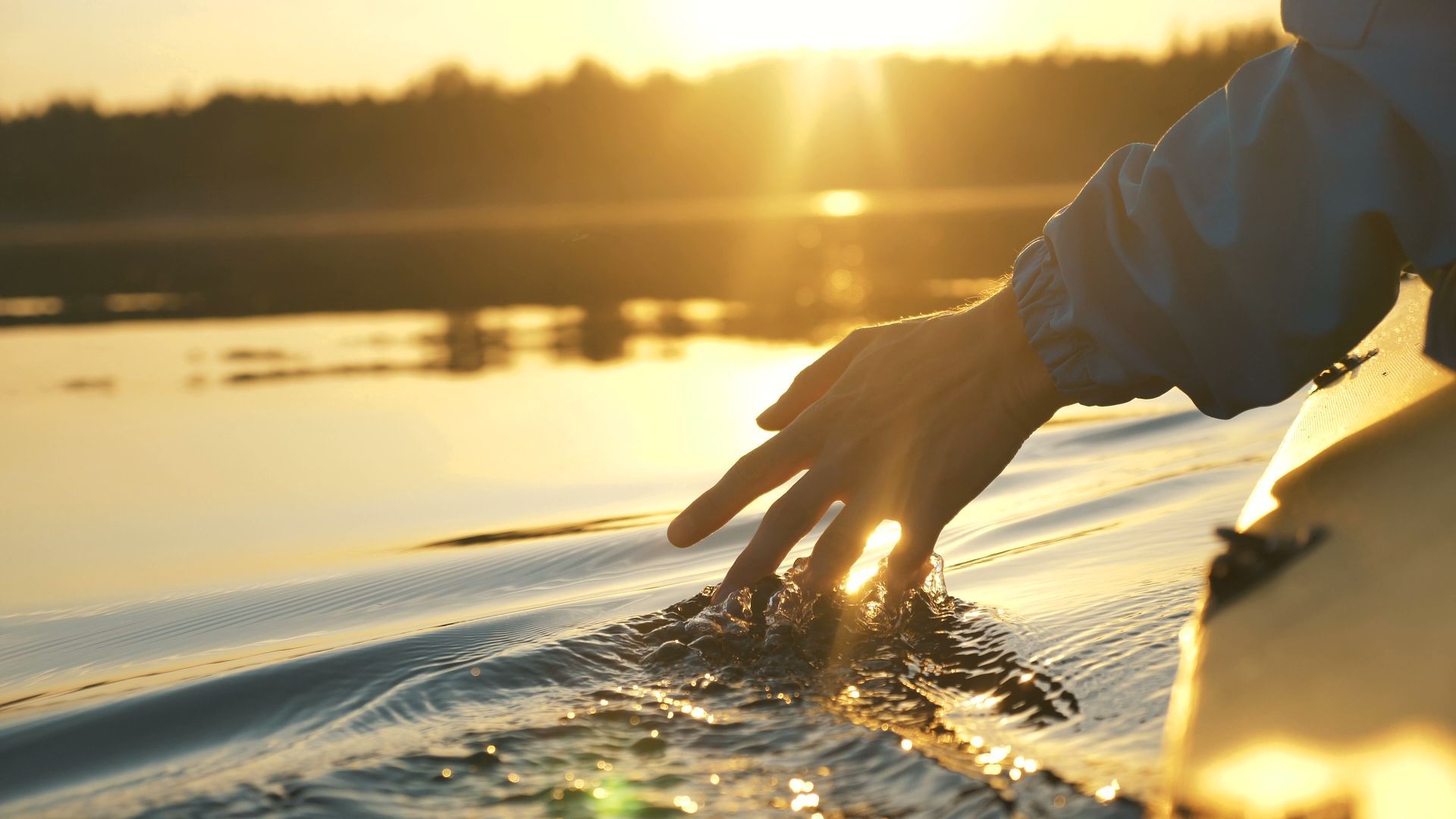 A person is touching the water with their hand at sunset.