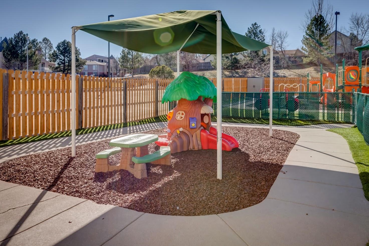 A playground with a tree house and a picnic table under an umbrella
