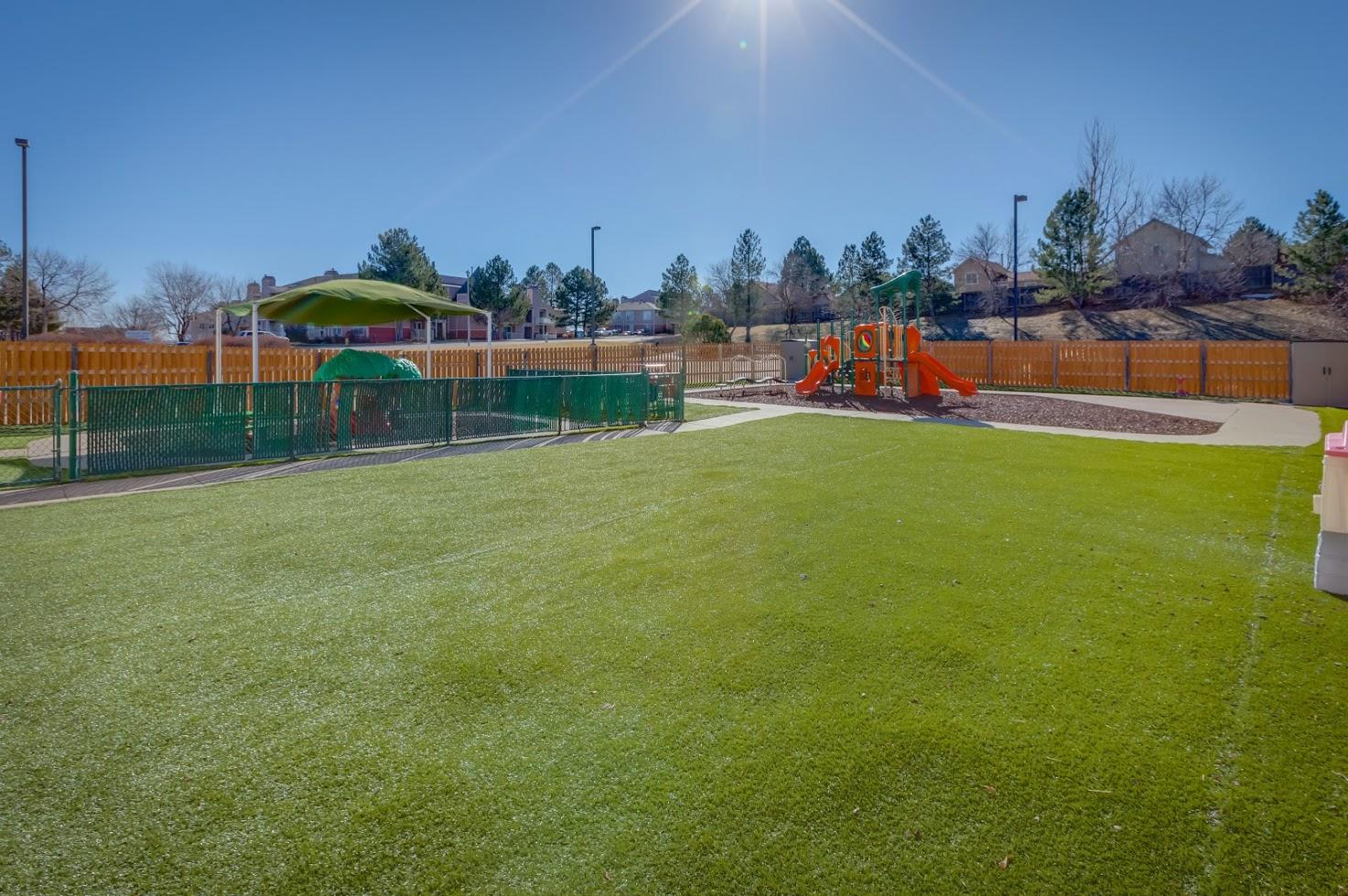 A large lush green field with a playground in the background.