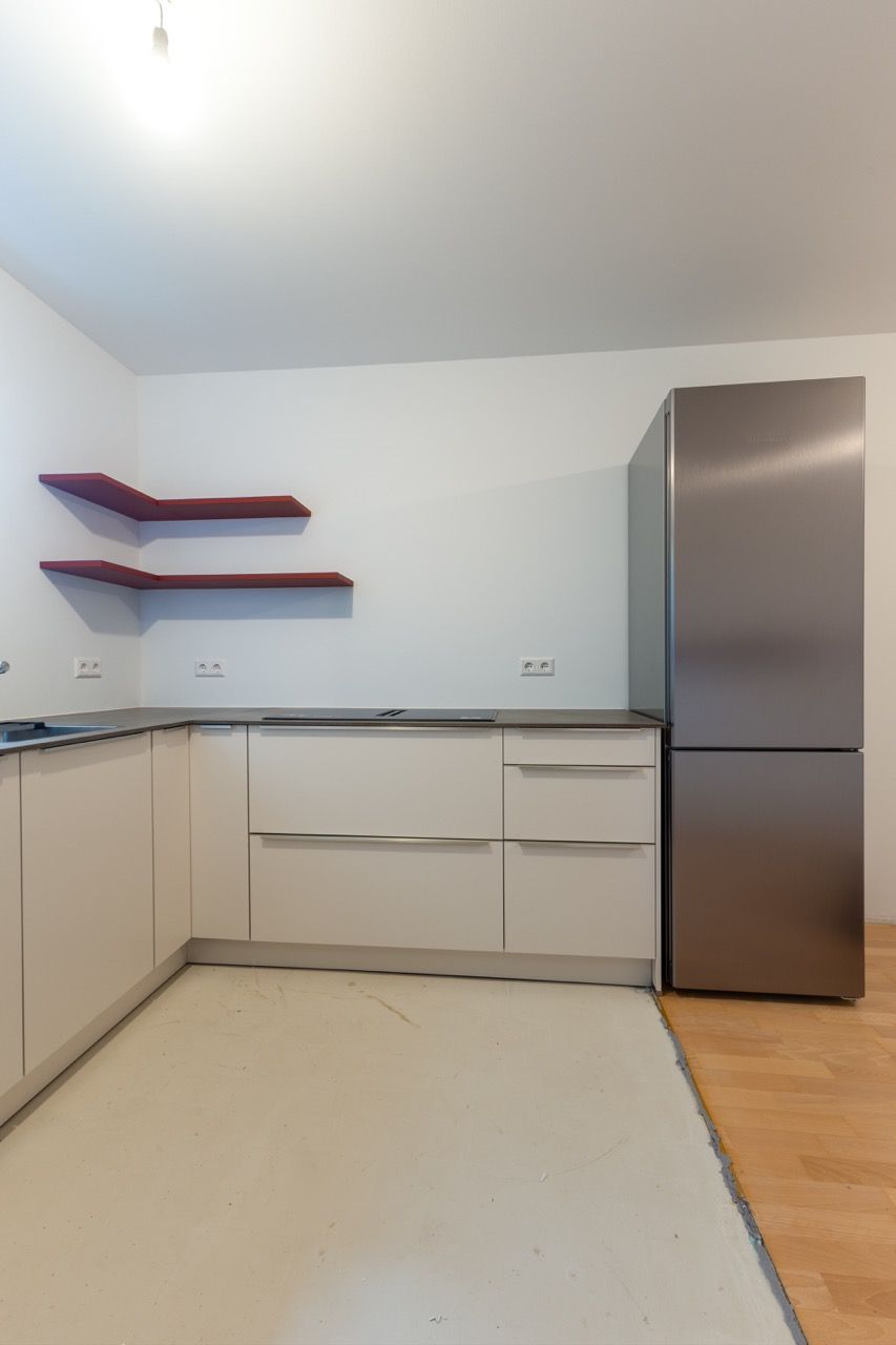 Minimalistische, moderne Küche mit weißen Schränken, grauer Arbeitsplatte, offenen Regalen und einem Edelstahlkühlschrank.