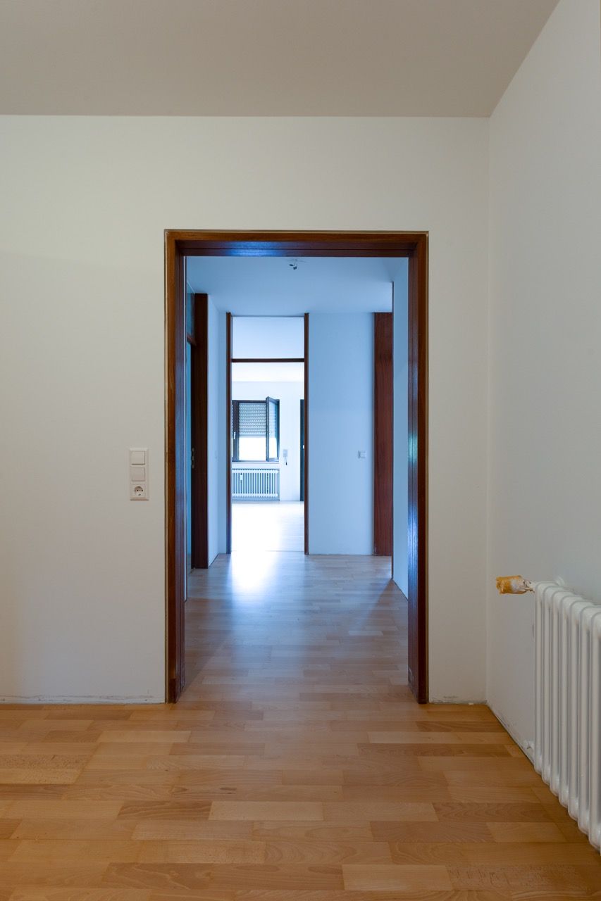 Leerer Flur mit Holzboden, weißen Wänden, einer Tür und einem Heizkörper auf der rechten Seite.