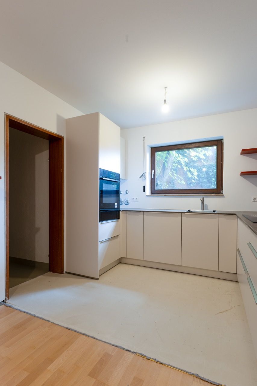 Helle, moderne Küche mit weißen Schränken, Holzboden und einem Fenster über der Spüle.