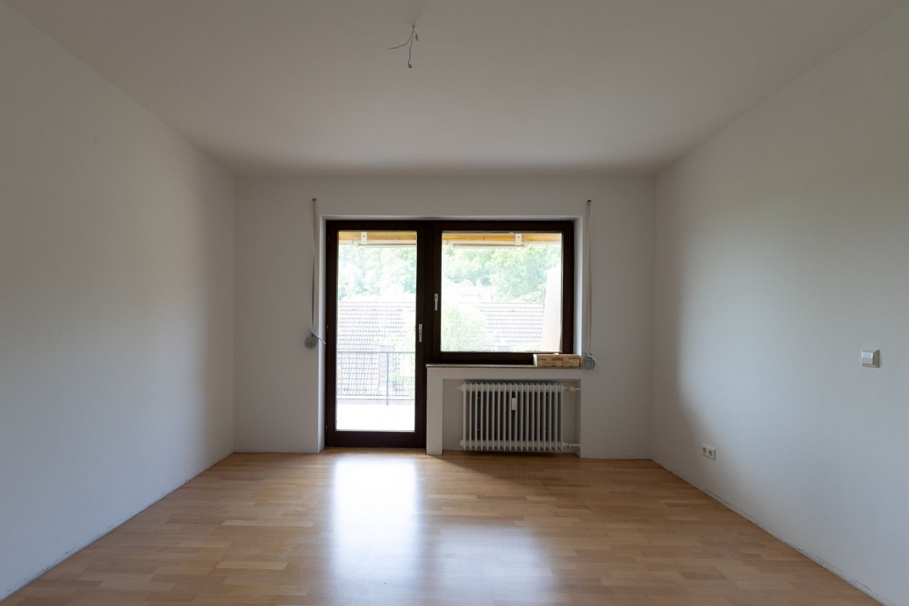 Leeres, unmöbliertes Zimmer mit Holzboden, weißen Wänden und einer Glastür und einem Glasfenster am anderen Ende.