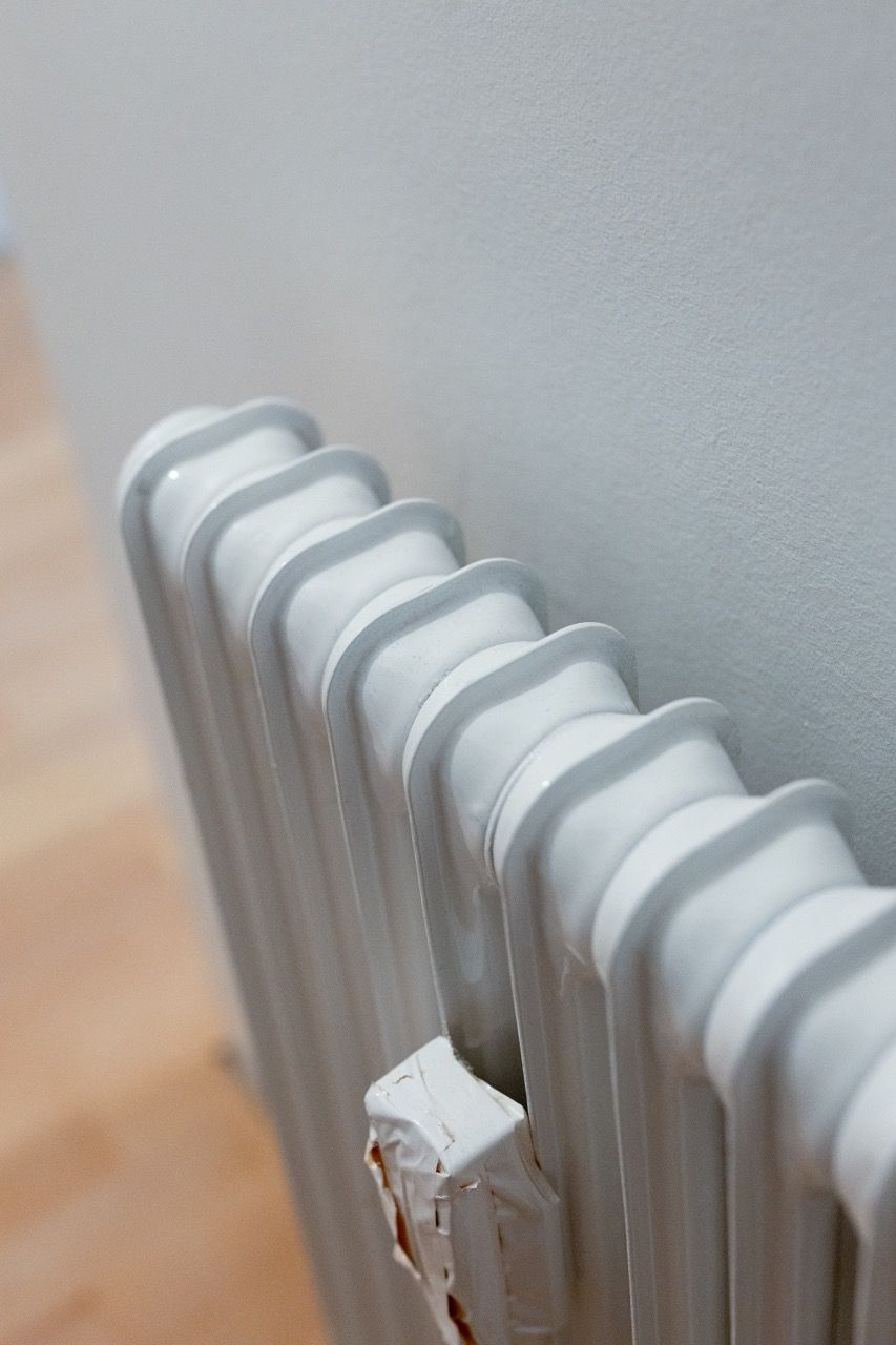 Weißer Heizkörper vor einer hellgrauen Wand mit einem abgenutzten Ventilknopf im Vordergrund