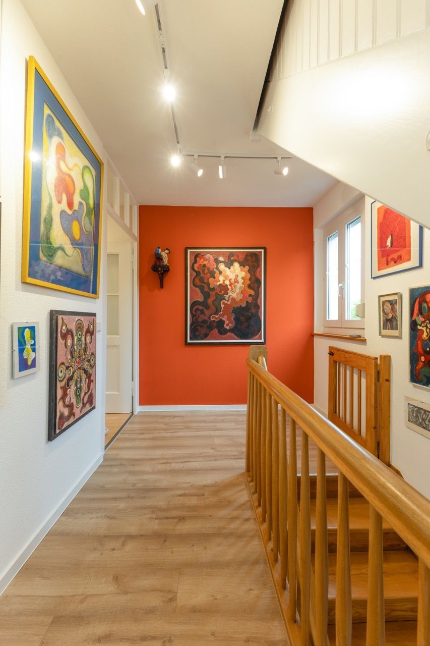 Flur einer Kunstgalerie mit orangefarbenen Wänden, gerahmten Gemälden und einem Holzgeländer unter Schienenbeleuchtung