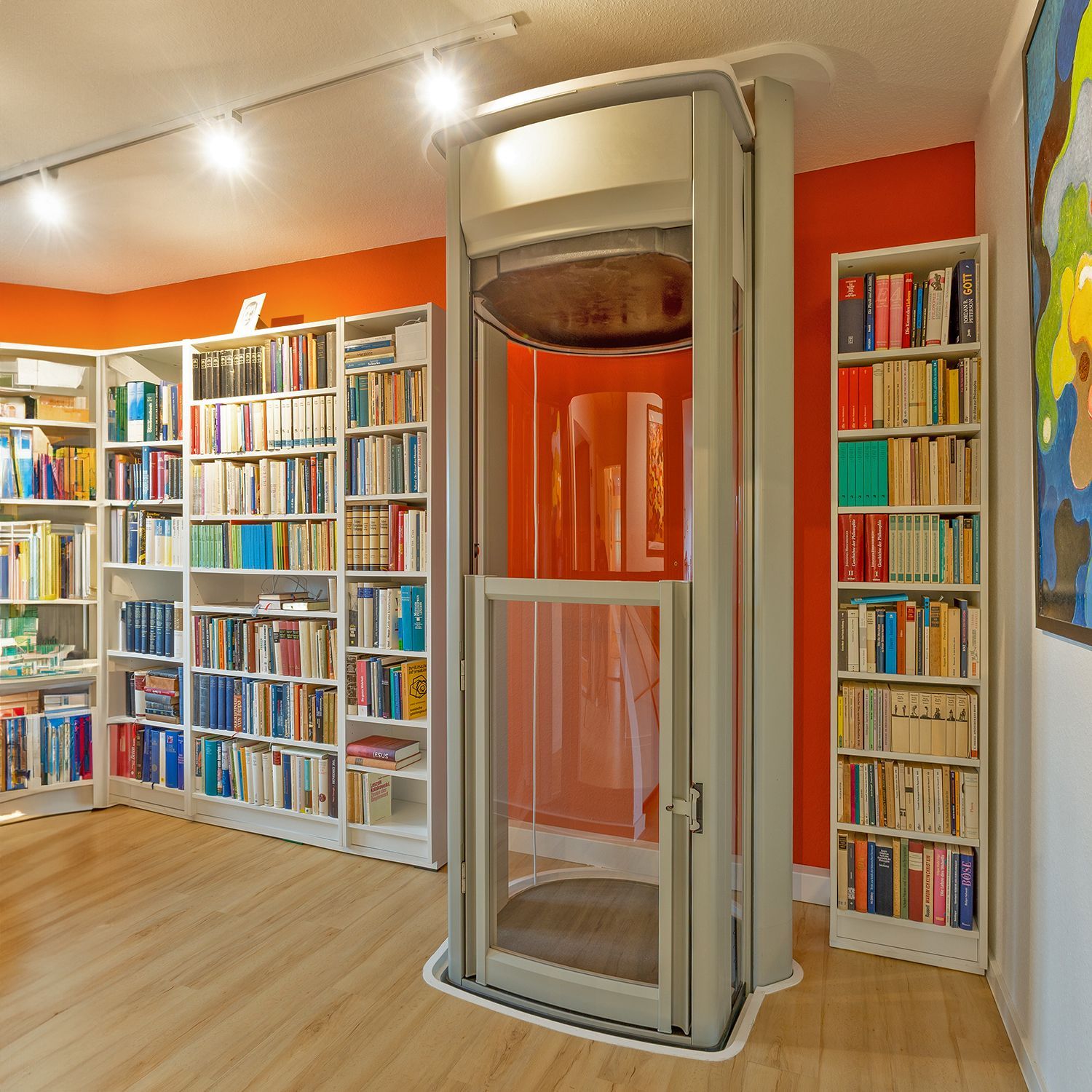 Modernes Bibliotheksinterieur mit raumhohen Bücherregalen und einem gläsernen Aufzug in der Mitte.