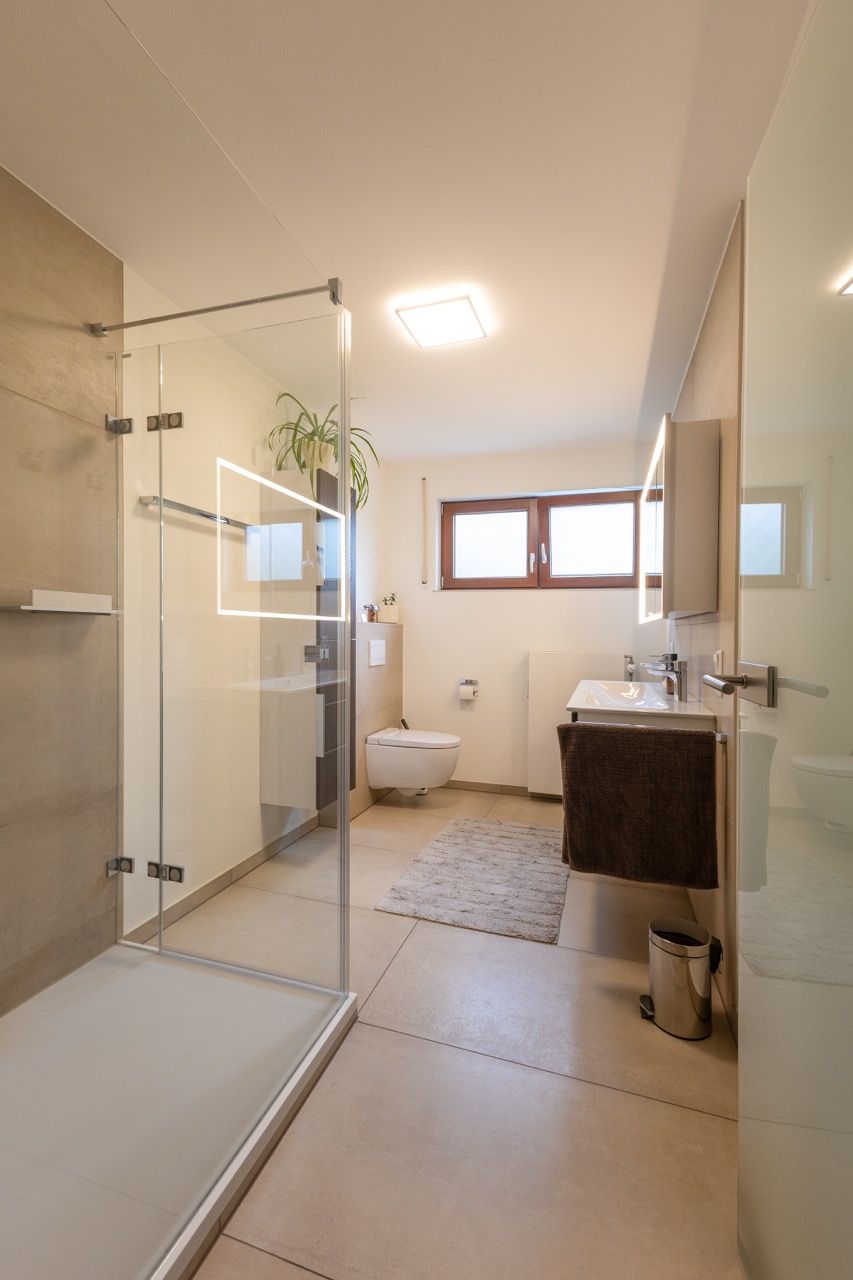 Modernes Badezimmer mit Glasdusche, WC, Waschbecken, Fenster und gewebtem Teppich