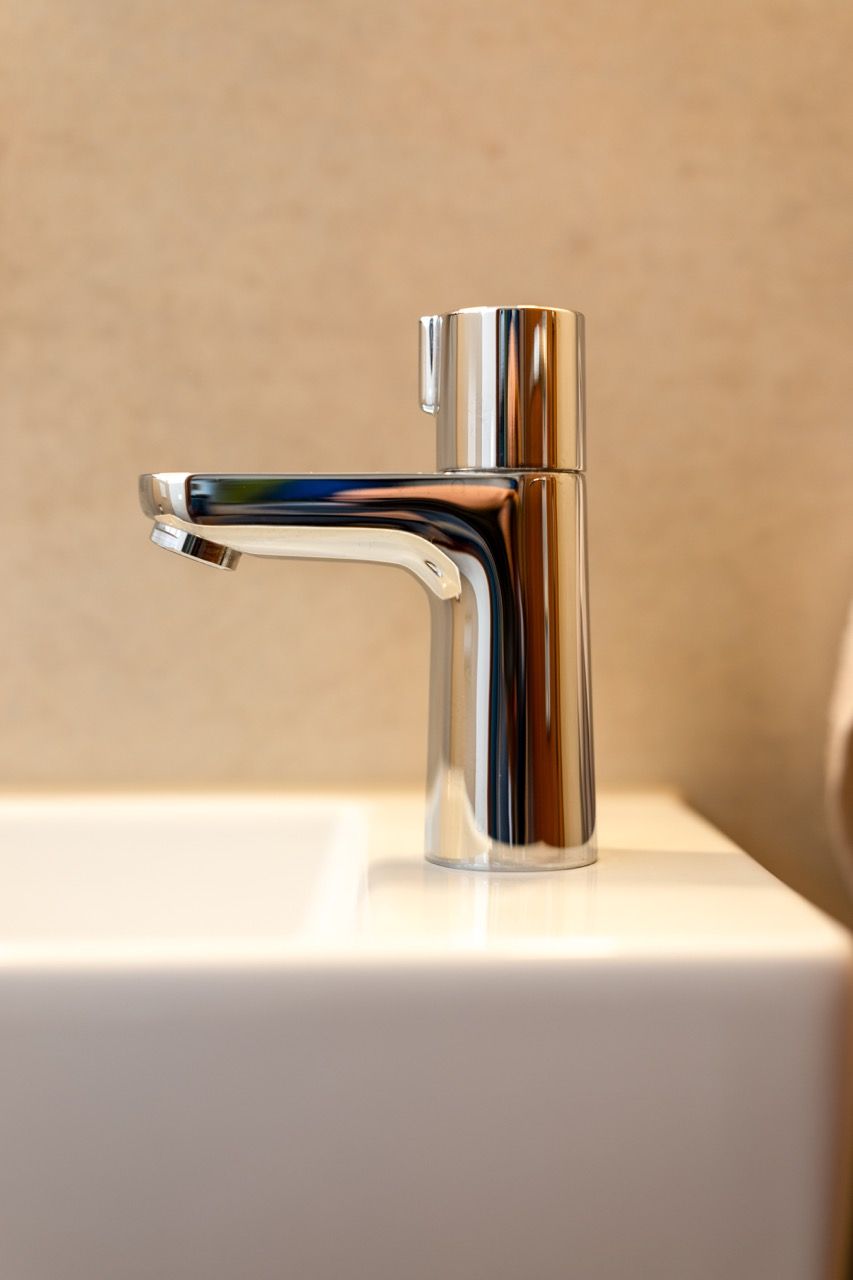 Verchromter Badezimmerhahn auf einem weißen Waschbecken vor einer beigen Wand