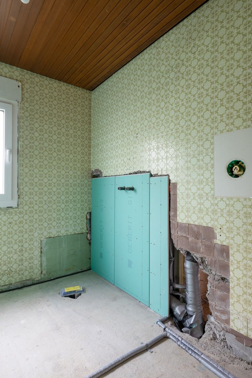 Altes Zimmerinterieur mit mintgrünen Schränken, zerrissener Tapete, freiliegenden Rohren und einer schrägen Holzdecke.