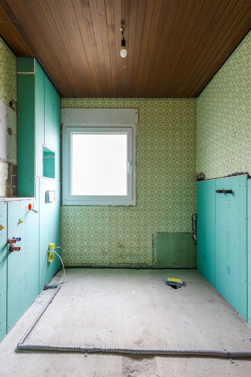Kleines Badezimmer mit grün gemusterten Wänden, Holzdecke, weißem Fenster und erhöhtem gefliestem Bodenbereich.