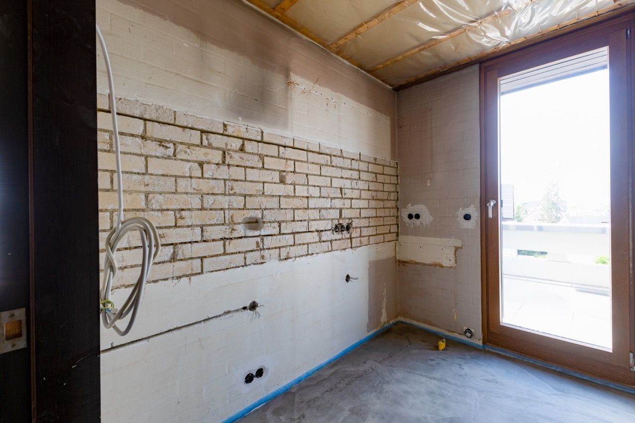 Renoviertes Zimmer mit freiliegender Ziegelwand, unfertigem Boden und Glastür, die Tageslicht hereinlässt