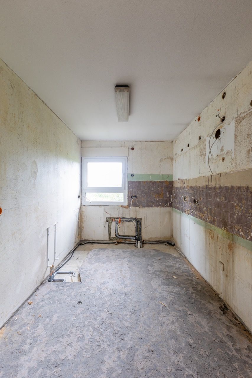 Ein leerer, abgewohnter Raum mit abblätternder Farbe, einem Fenster und einer Leuchtstoffröhre an der Decke.