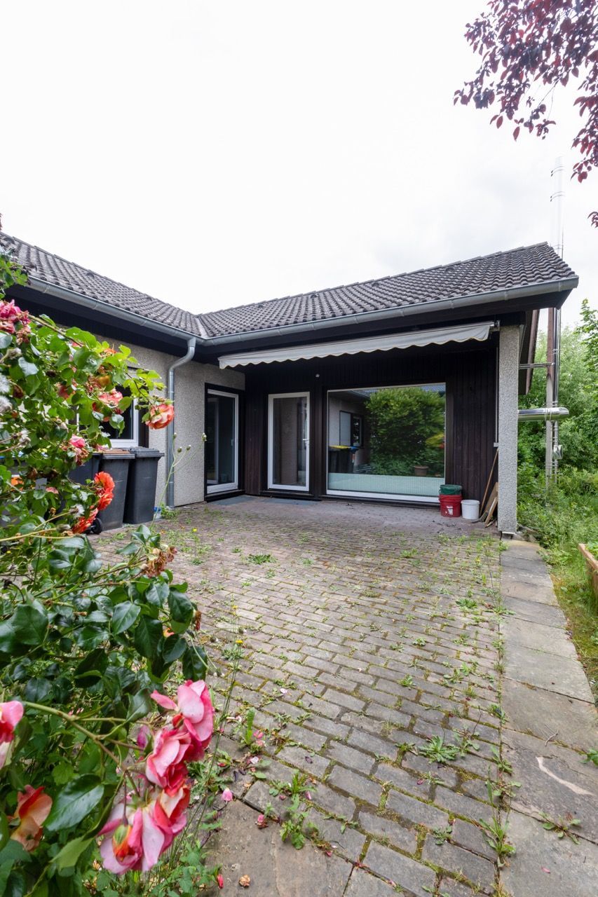 Modernes Hausäußeres mit gepflasterter Auffahrt, Veranda und blühenden Pflanzen im Vordergrund