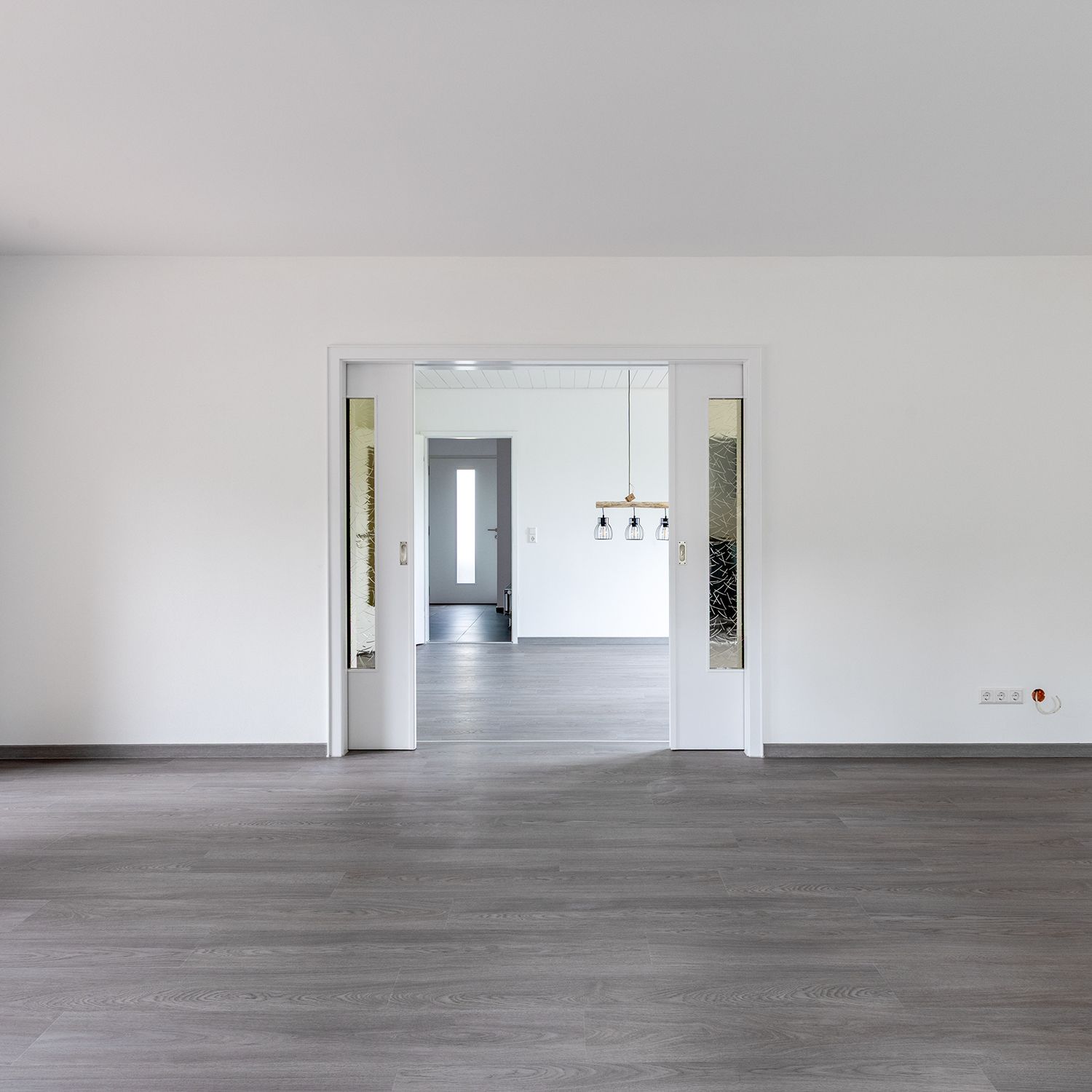 Verwilderter Vorgarten vor einem beigefarbenen zweistöckigen Haus mit Bäumen und Sträuchern.