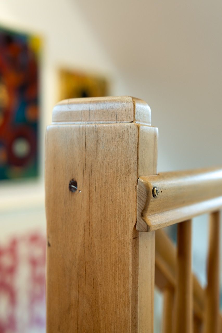 Nahaufnahme eines hellen Treppengeländerpfostens aus Holz mit verschwommenem Wandbild im Hintergrund