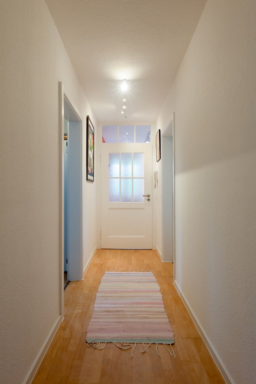 Schmaler Flur mit hellen Wänden, Holzboden, gestreiftem Läuferteppich und einer hellen Fenstertür am Ende.