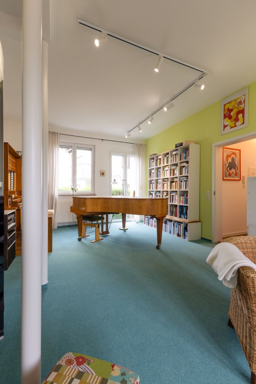 Helles Wohnzimmer mit blauem Teppich, Holztisch, Bücherregalen und Schienenbeleuchtung.