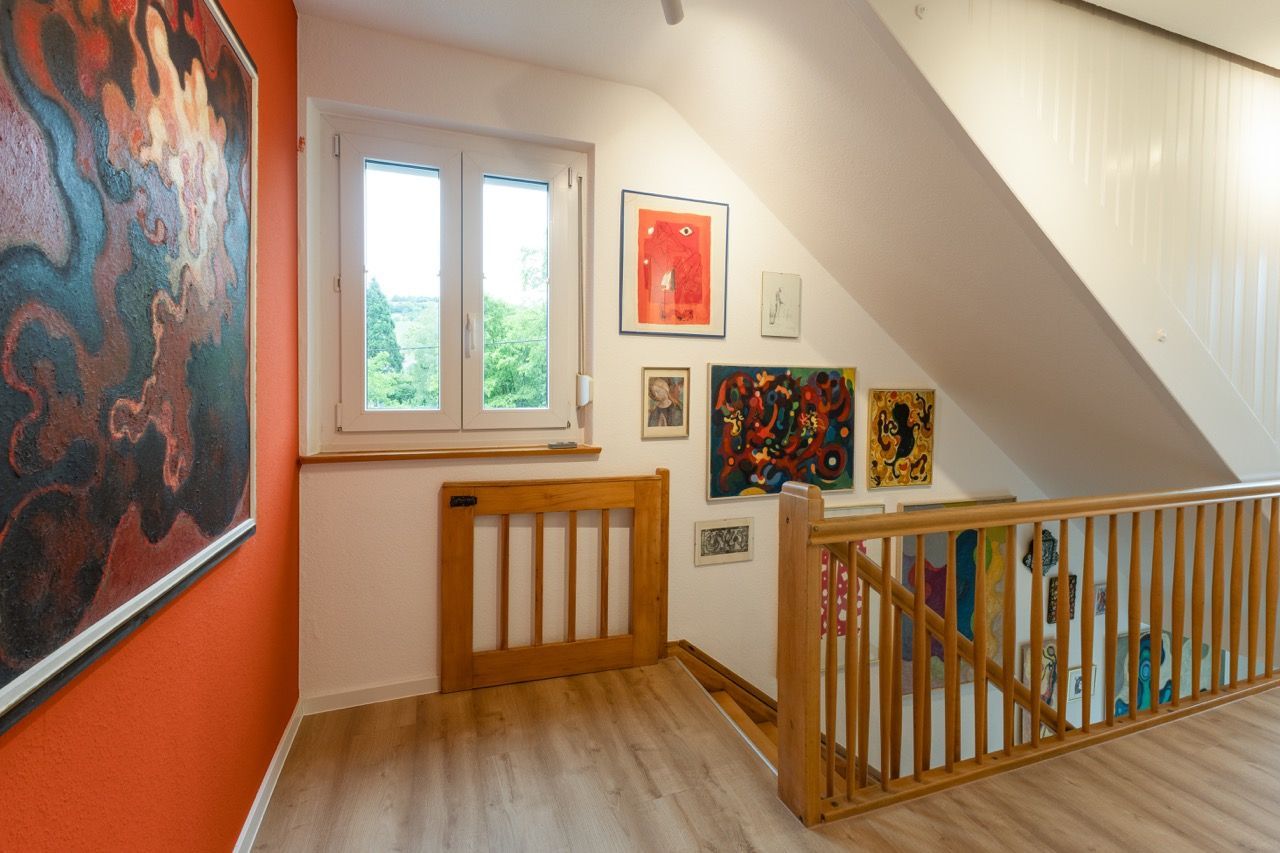 Heller Treppenabsatz mit farbenfroher Wandkunst, einem Fenster und einem Holzgeländer in einem modernen Interieur.