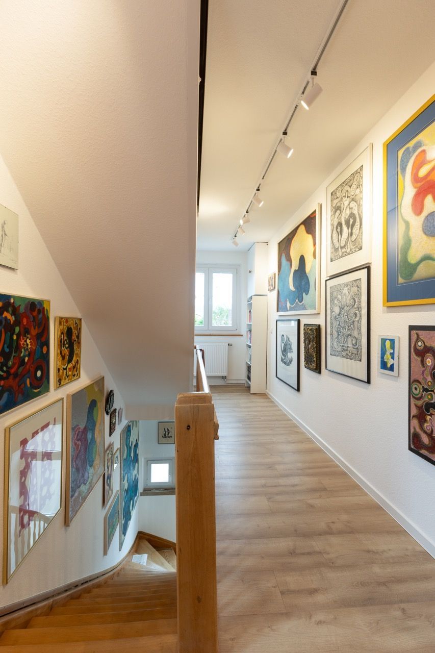 Heller Flur einer Kunstgalerie mit gerahmten Gemälden an weißen Wänden und Holzböden, beleuchtet durch Schienenbeleuchtung.