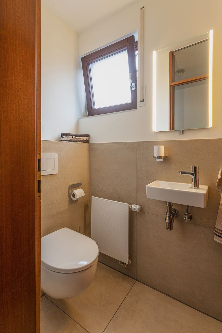 Modernes, barrierefreies Badezimmer mit wandhängendem WC, Waschbecken, Spiegel und kleinem Fenster
