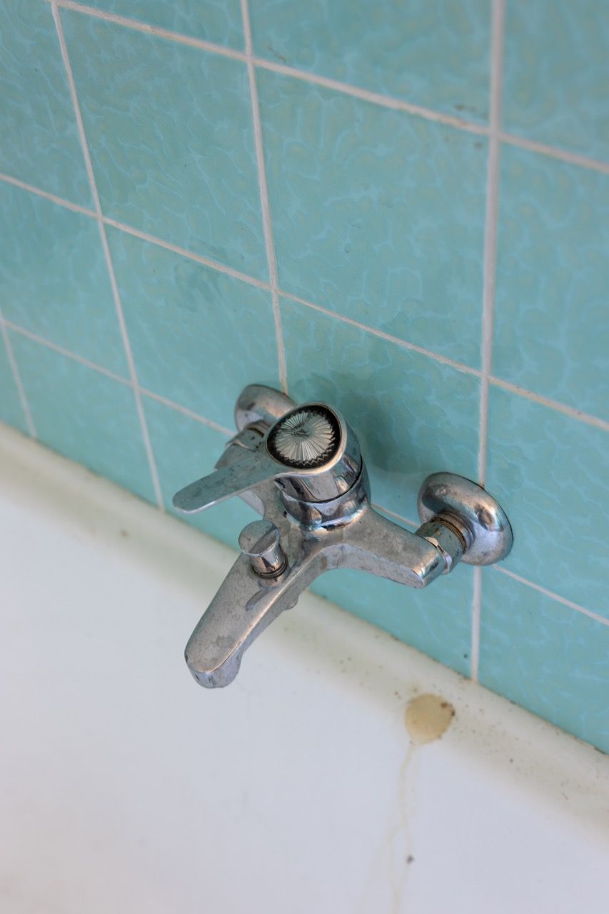 Verchromter Badewannenarmatur vor türkisfarbener Fliesenwand, Wasser tropft in die Badewanne