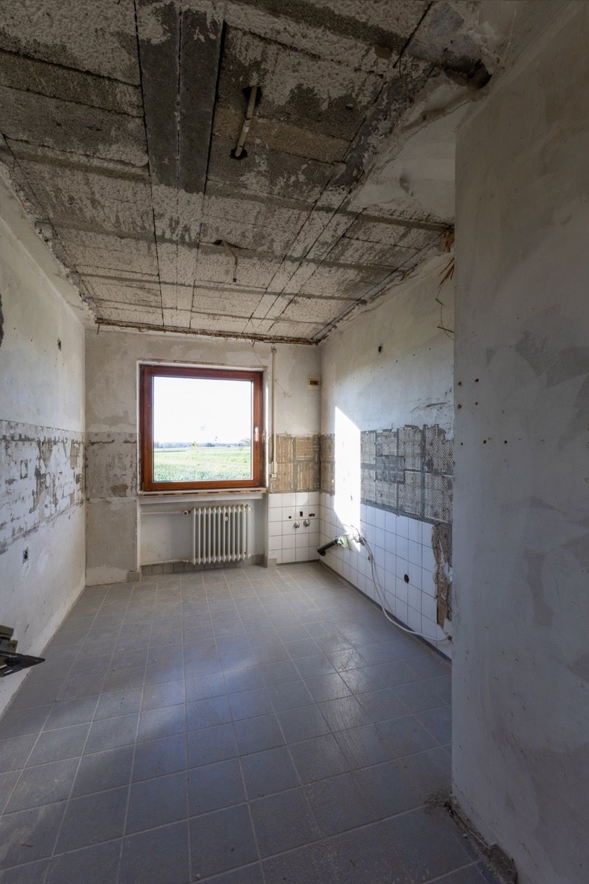Leerer, unfertiger Raum mit nackten Betonwänden, freiliegender Decke und einem Fenster über einem Heizkörper.