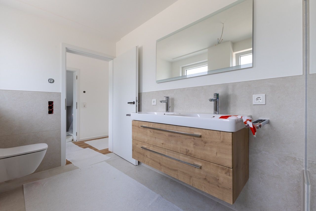 Modernes Badezimmer mit Waschtisch aus Holz, großem Spiegel und Badewanne in einem hellweißen Interieur