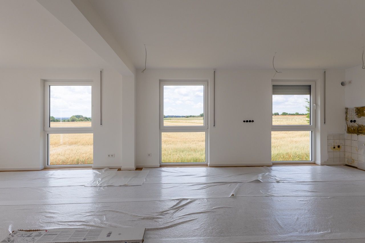 Leerer weißer Raum mit großen Fenstern und unfertigen Dielenböden mit Blick auf ein Feld