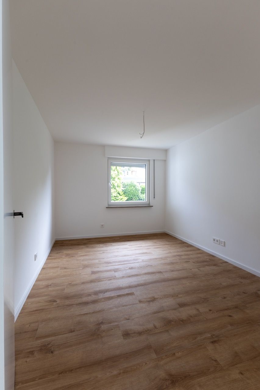 Leerer weißer Raum mit Holzboden und einem kleinen Fenster mit Blick ins Grüne draußen