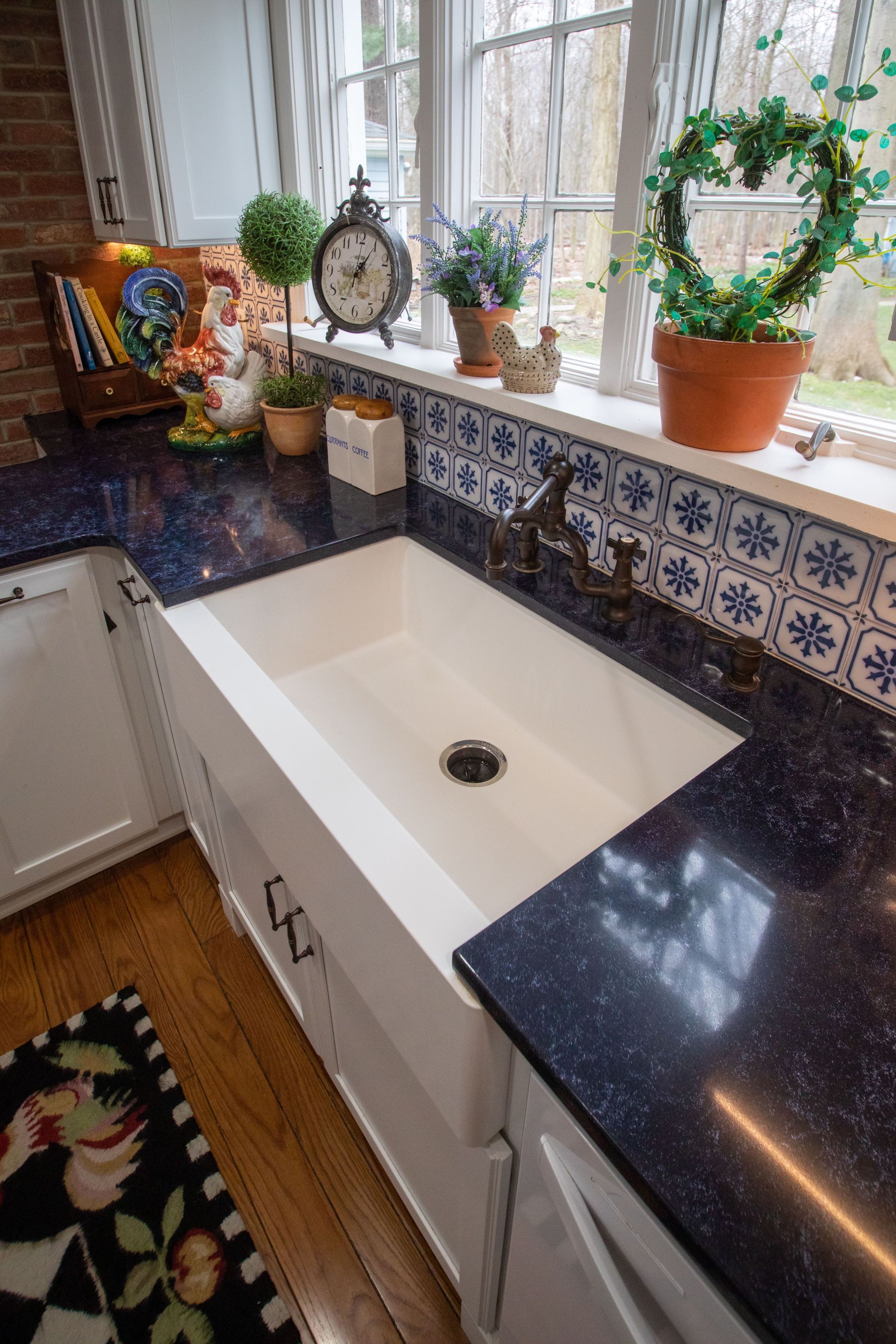 White farmhouse sink in a kitchen with blue speckled countertops, window.