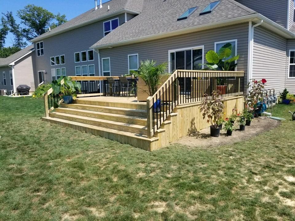 Wooden deck with steps leading to a house, with potted plants and black railings.