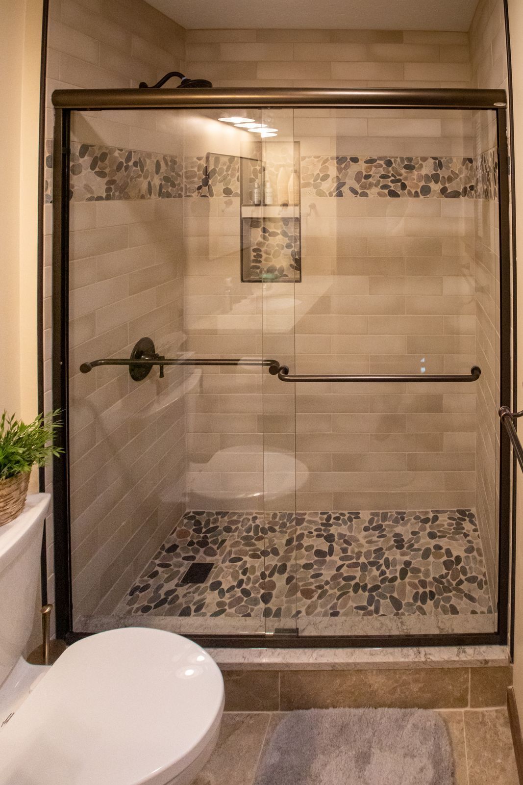 Shower with glass door, brown frame, stone tile floor, and mosaic tile accent.