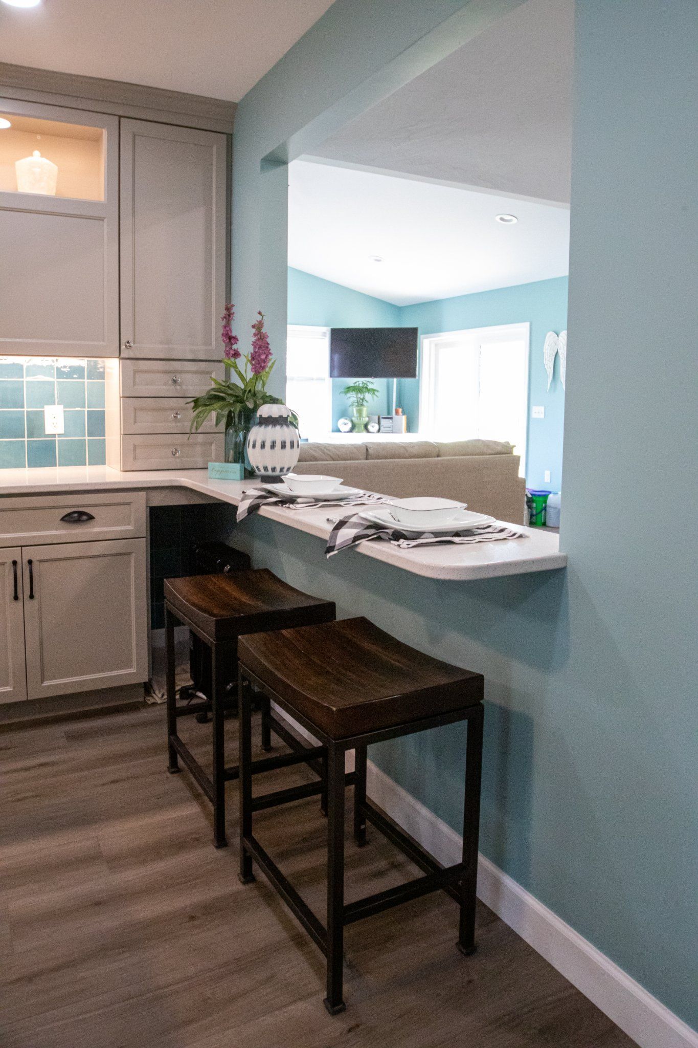 Kitchen with a bar, two stools, and a light blue wall. Dark wooden stools, gray cabinets.