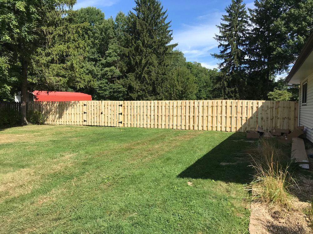 A wooden fence encloses a grassy backyard, adjacent to a house under a blue sky.