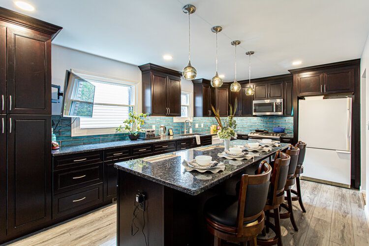Dark wood kitchen with granite island and bar seating. Blue-green backsplash and pendant lights.