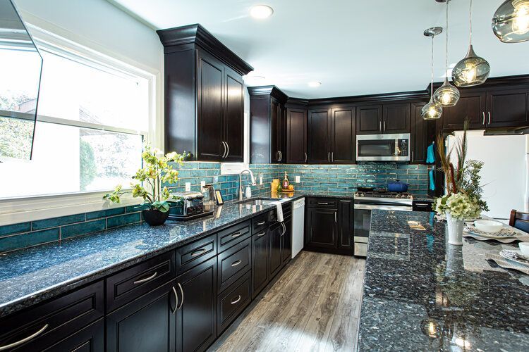 Dark kitchen with blue backsplash and countertops, dark cabinets, light wood floor, and pendant lights.
