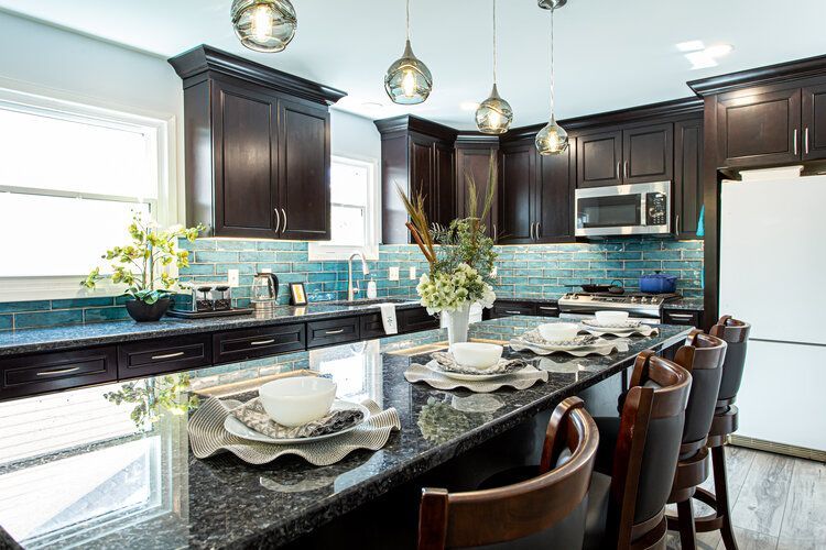 Kitchen with dark brown cabinets, blue backsplash, granite island, and pendant lights.