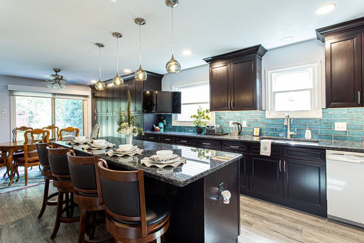 Modern kitchen with dark cabinetry, granite island with bar stools, and dining area.