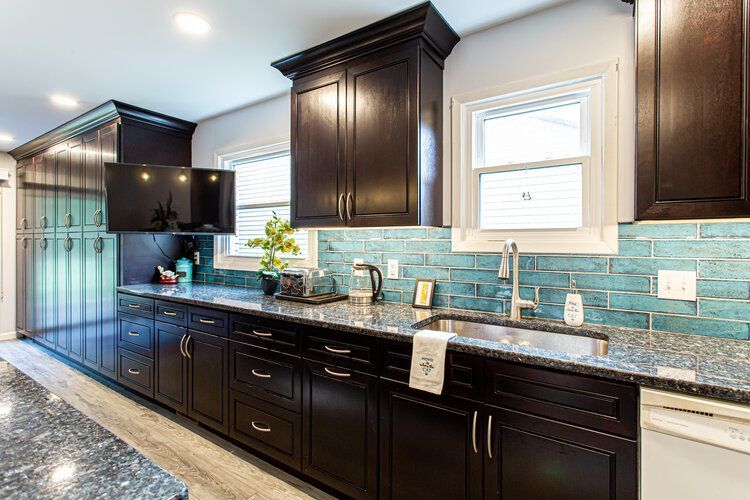 Dark wood kitchen cabinets with a blue tile backsplash, granite countertop, and a stainless steel sink.