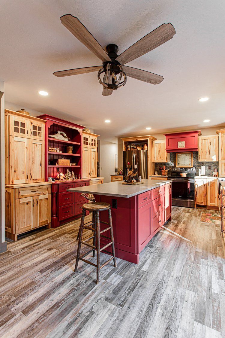 Kitchen with red island, natural wood cabinets, and a wooden floor. A dark-colored ceiling fan is overhead.