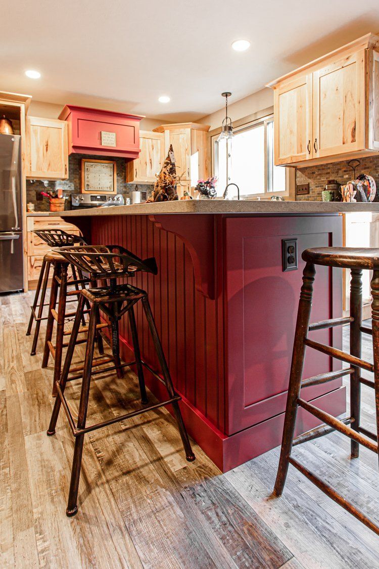 Kitchen with red island, wood cabinets, and bar stools; neutral flooring.