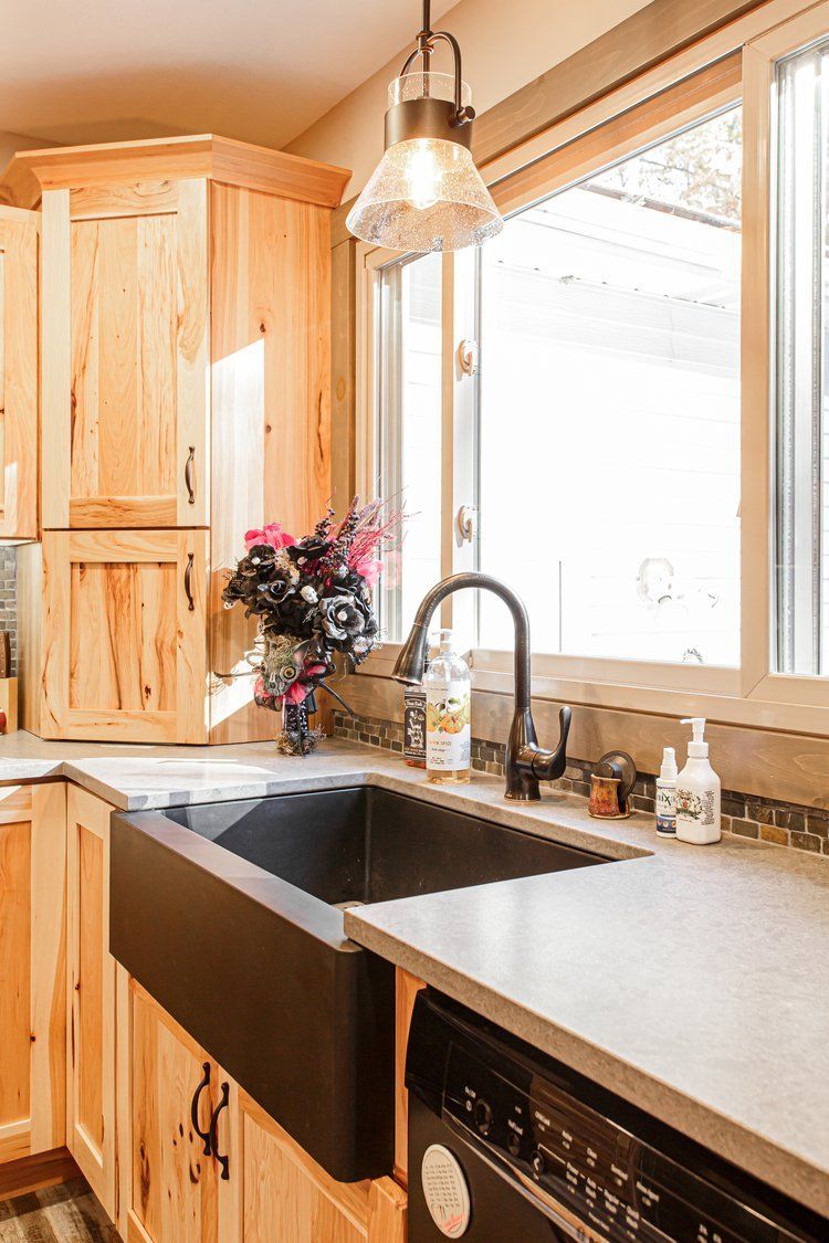 Kitchen sink with black apron sink, wood cabinets, and large window.