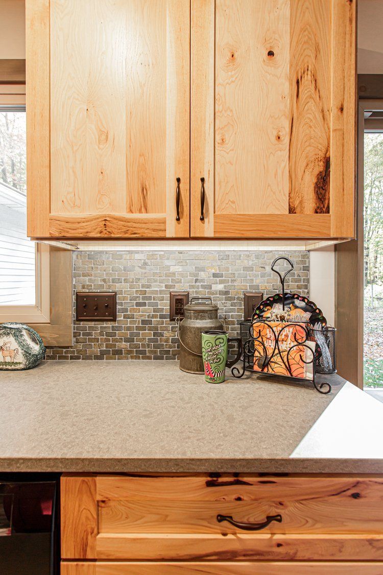 Wooden kitchen cabinets above a gray countertop, with decorative items and a tiled backsplash.